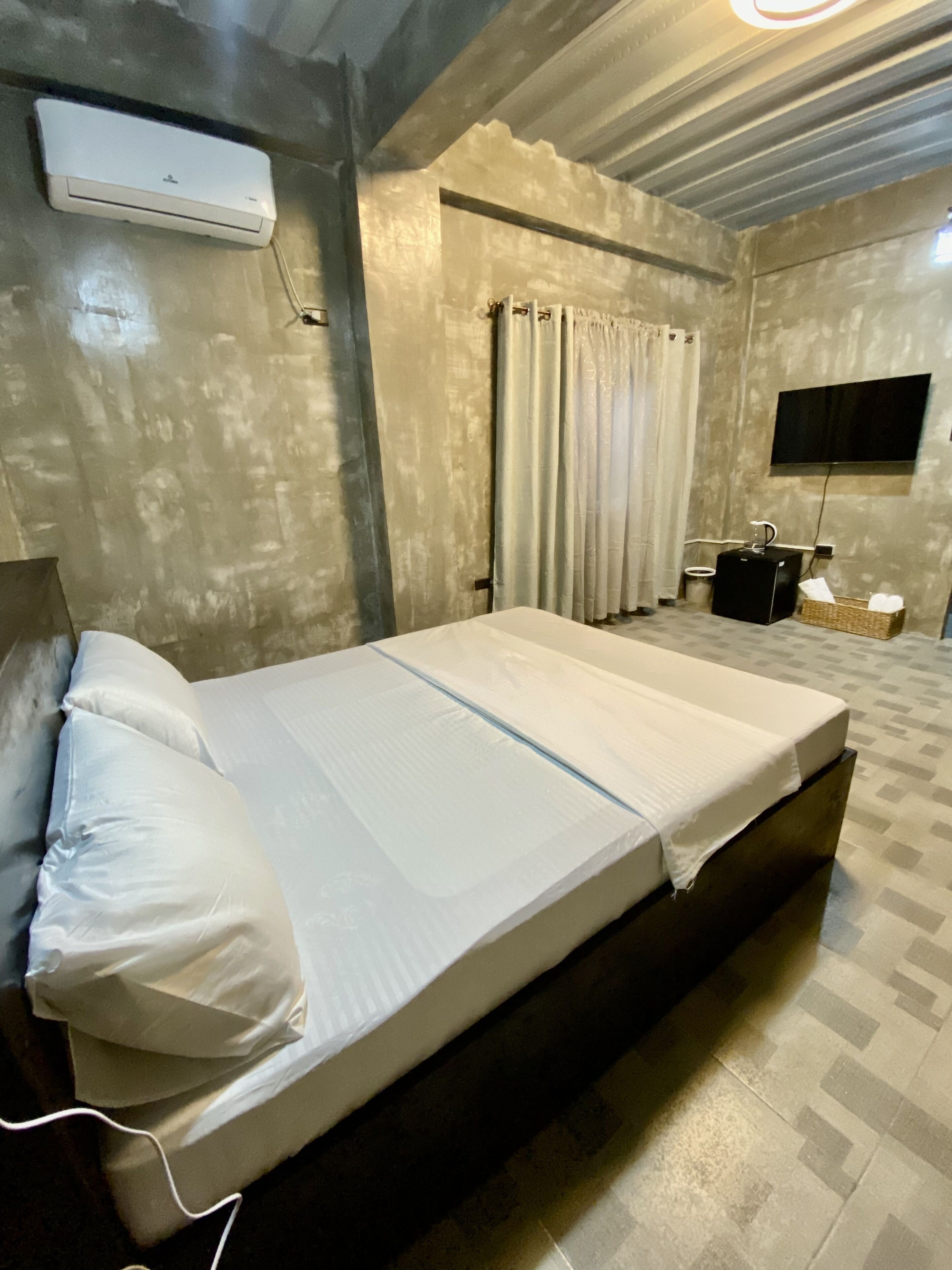 A bedroom with a bed, curtains, a TV, and an air conditioning unit.