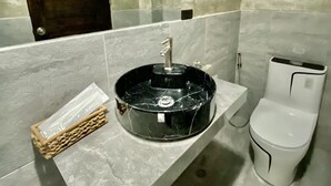 A bathroom with a marble sink, a mirror, a toilet, and a small wicker basket.