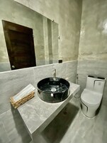 A bathroom with a marble sink, a mirror, a toilet, and a small wicker basket.