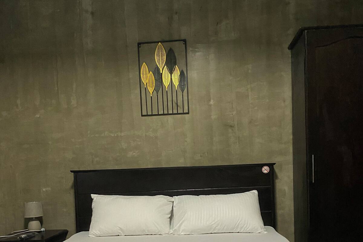 A neatly made bed with white linens in a room with a concrete wall and a dark wooden headboard.
