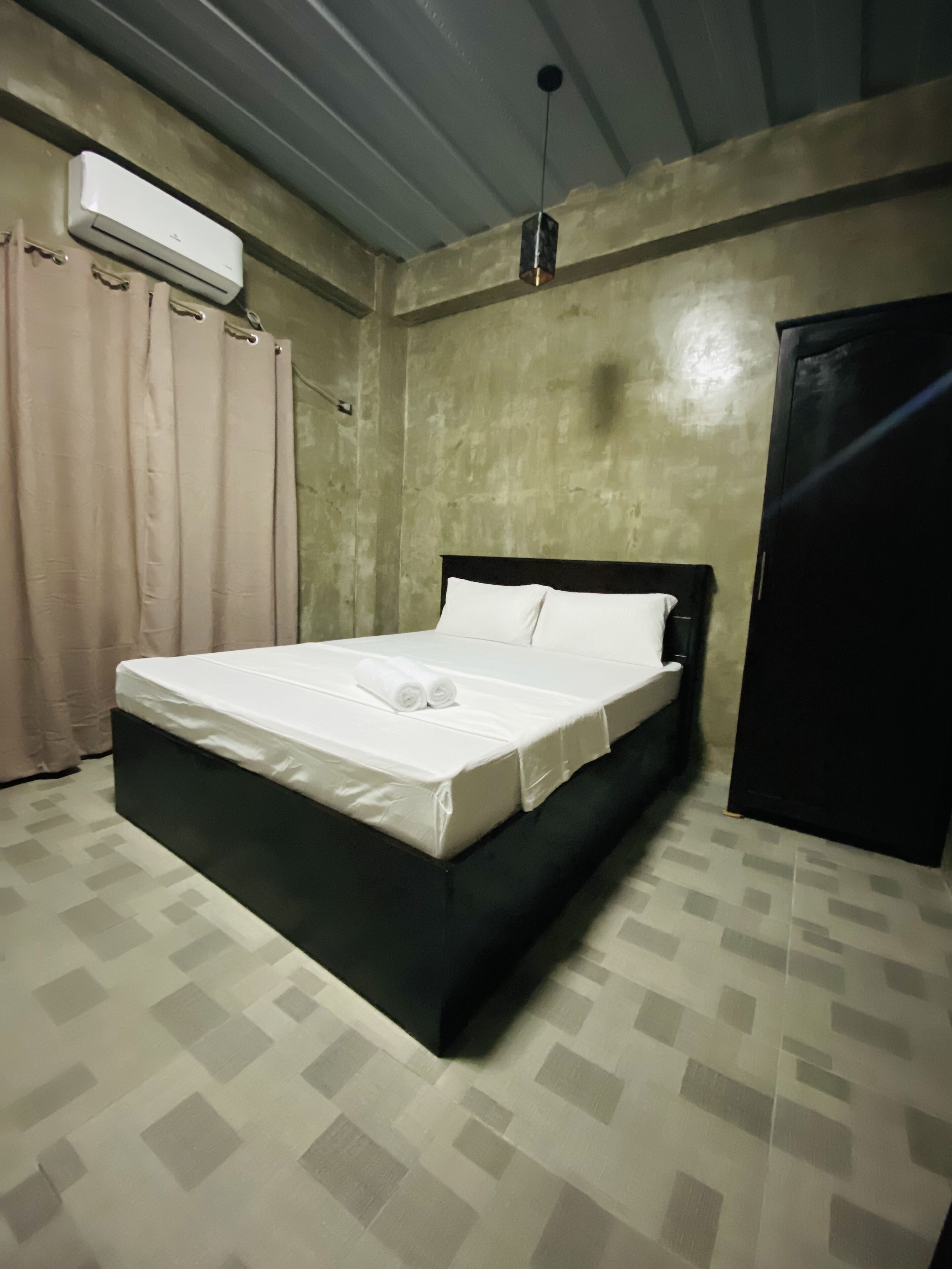 Uma cama de solteiro com roupa de cama branca, cabeceira preta e ventoinha de teto.