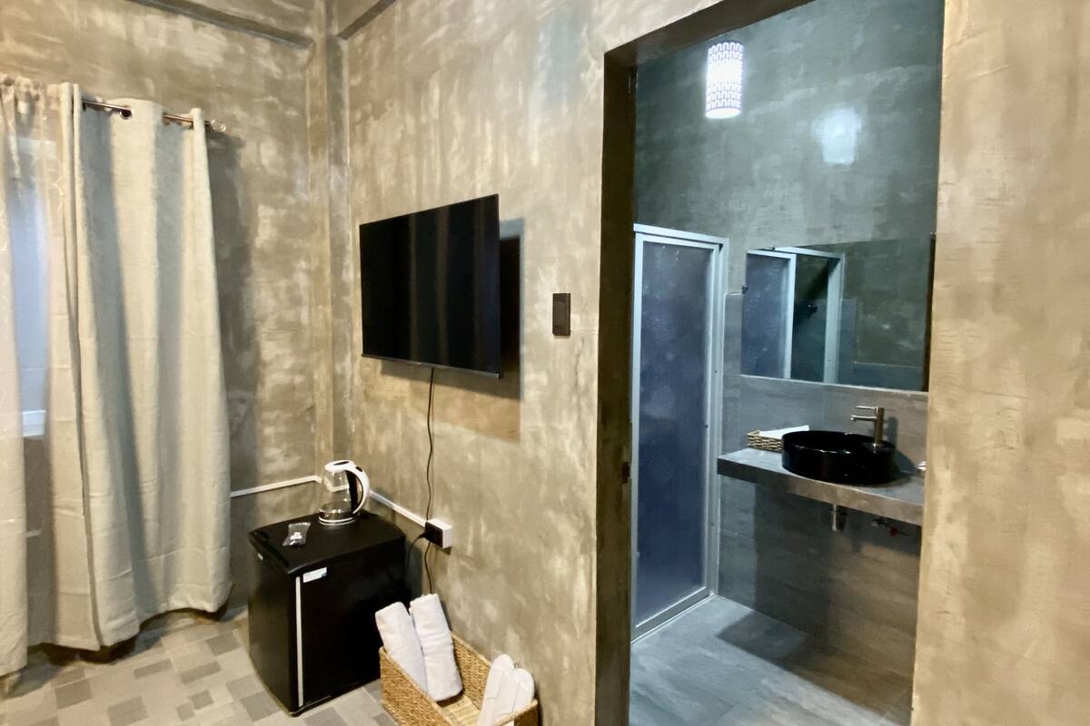 A bathroom with a shower, a sink, a mirror, a television mounted on the wall, and a towel rack with towels.