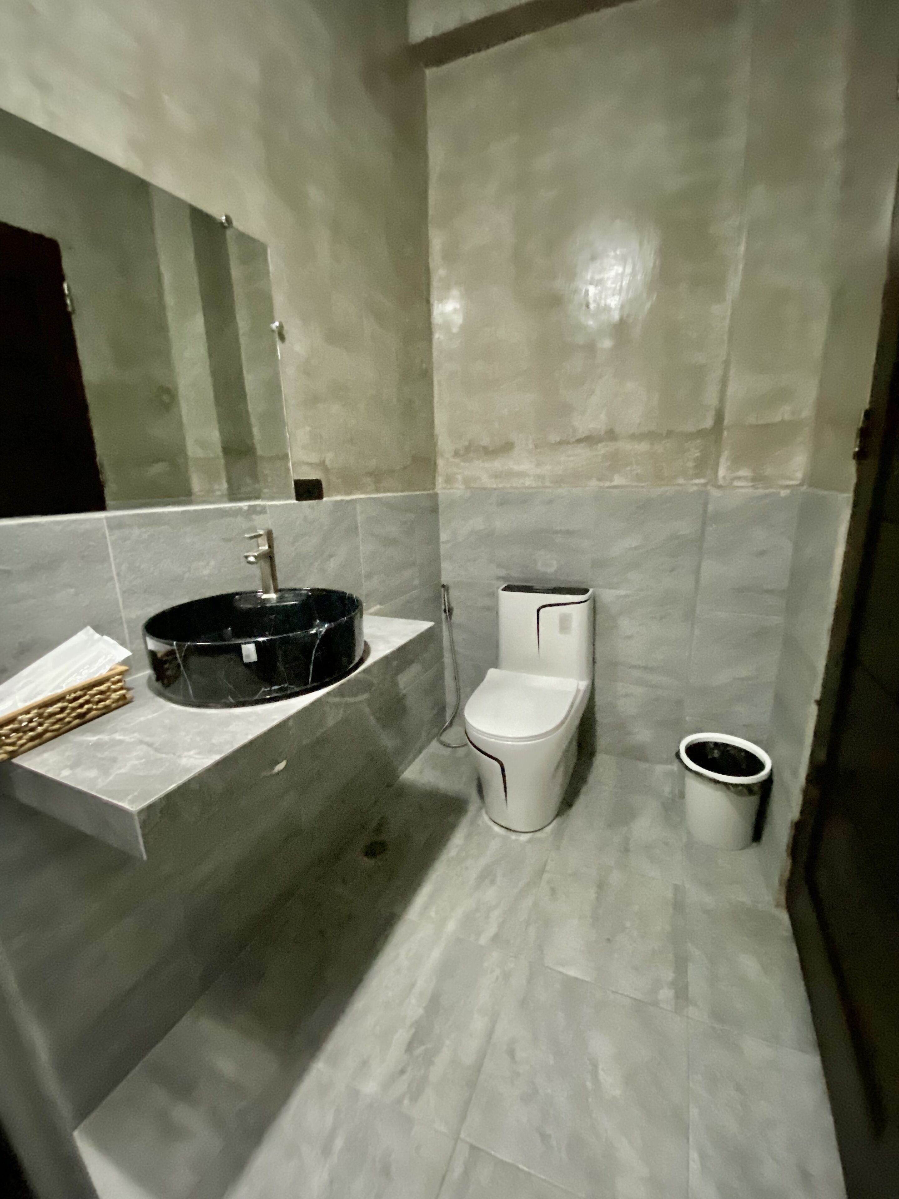 Un baño con un lavamanos negro, un inodoro blanco y un cubo de basura.