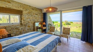 Ein Schlafzimmer mit Steinsturz, einem großen Bett mit gestreifter Bettwäsche, einem Schreibtisch mit Lampe und Blick ins Freie.