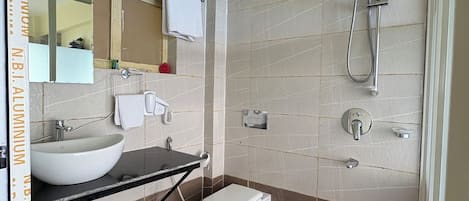 Un baño con lavamanos, espejo, inodoro, ducha y un cubo rojo.