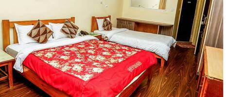A double bed with a red floral bedspread and two pillows, a wooden nightstand, a wooden wardrobe, and a mirror on the wall.