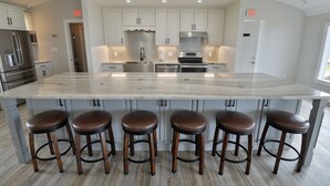 Une cuisine moderne avec des armoires blanches, des appareils en acier inoxydable et un grand îlot central doté de tabourets de bar.