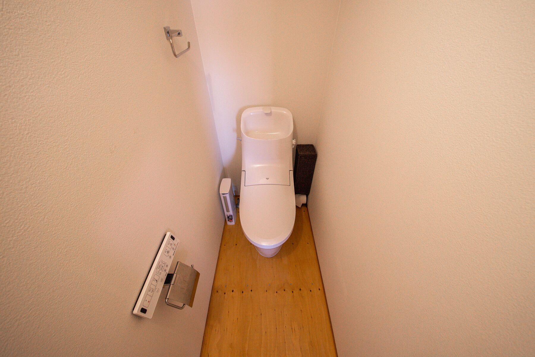 A small, narrow bathroom with a white toilet, a wall-mounted paper towel dispenser, and a toilet paper holder.