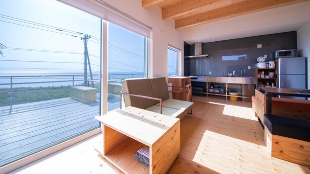 A modern interior with a wooden deck, large windows, a kitchen area, and a seating area with a table and chairs. - SUNNY SIDE HOUSE (Ishikari)