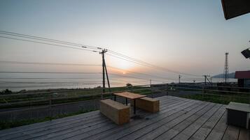 A wooden deck with a table and benches, overlooking a road and power lines, with a sunset in the background.
