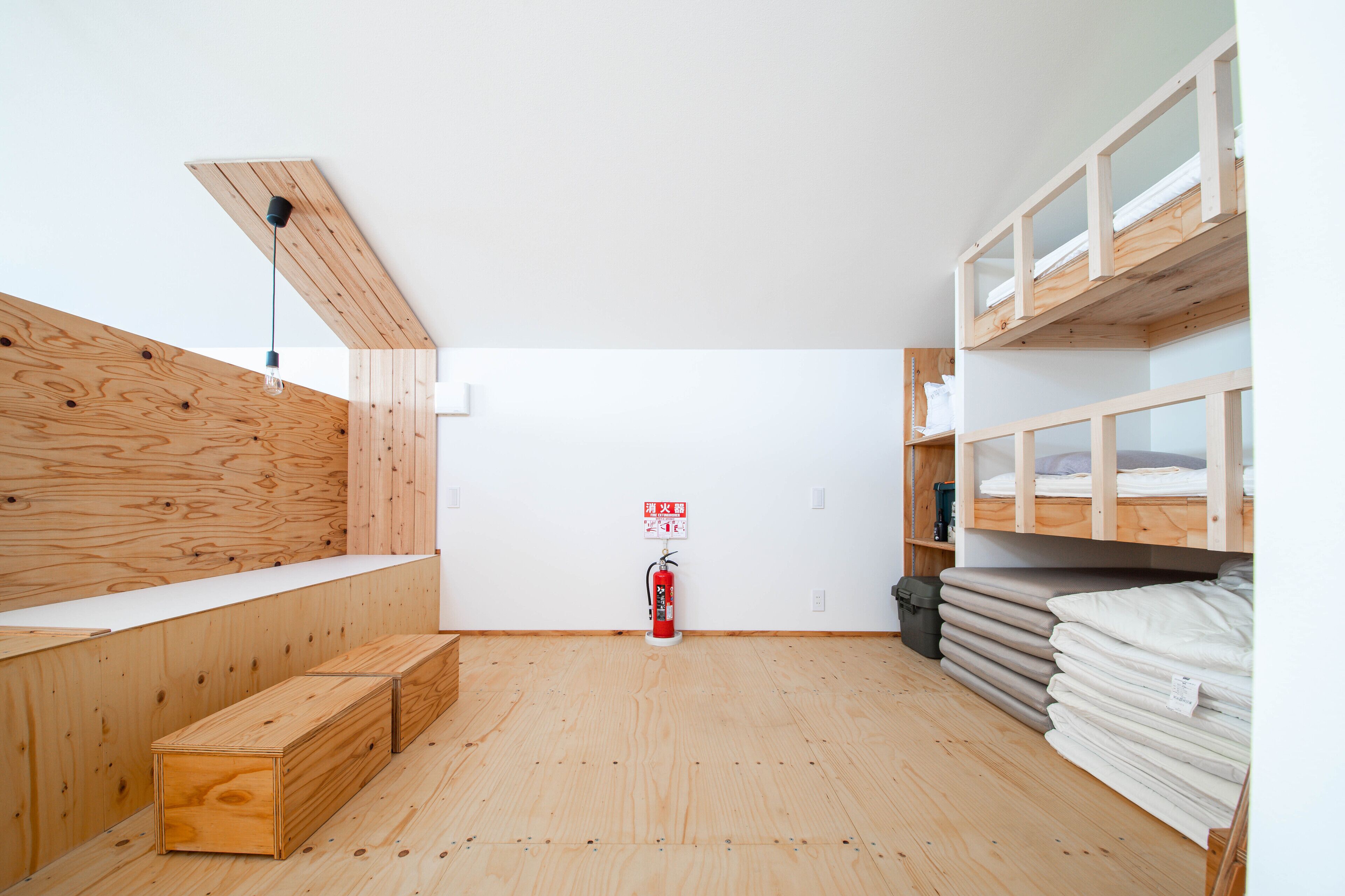 A room with wooden walls and floors, a fire extinguisher, and bunk beds with mattresses.