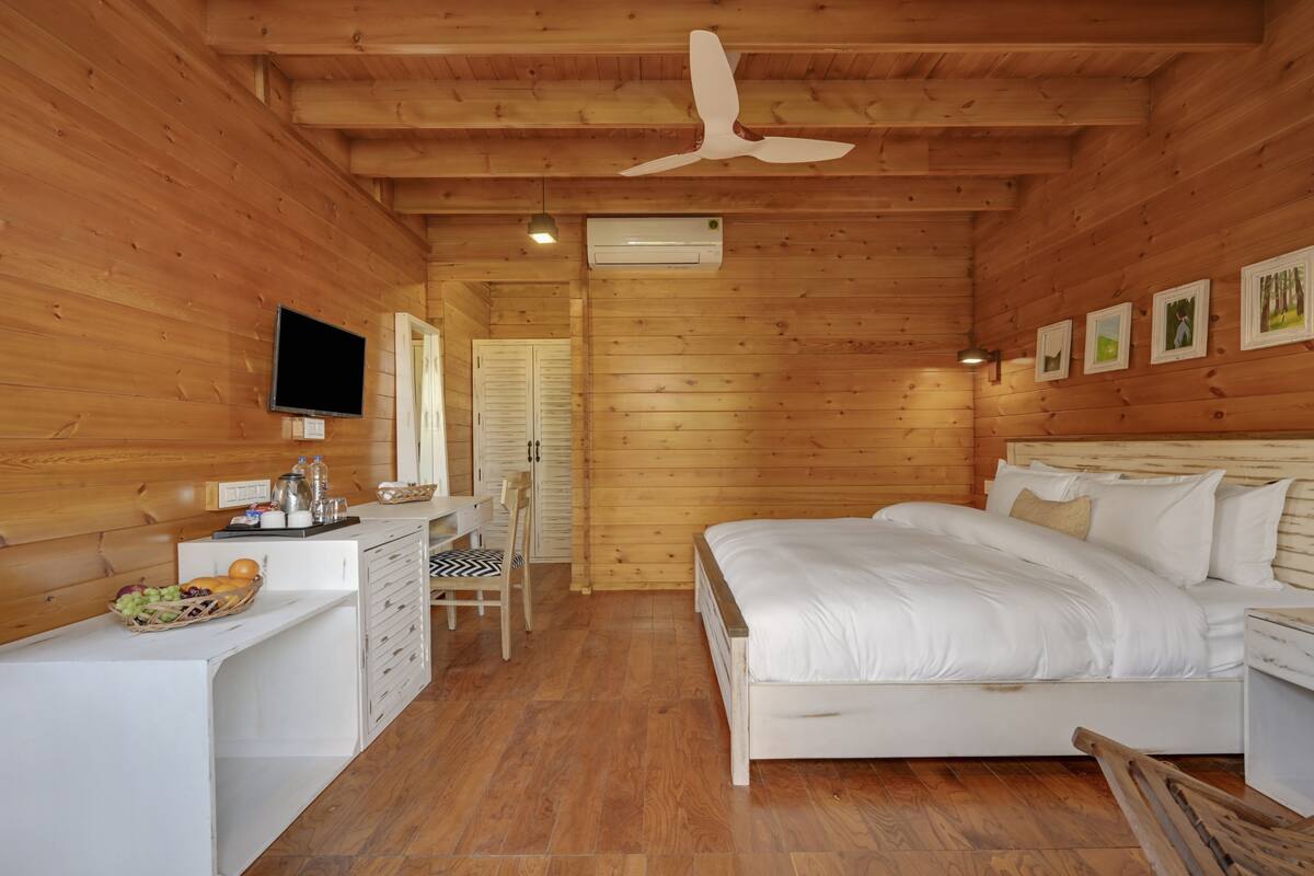 Een houten slaapkamer met een bed, bureau, stoel en een televisie.