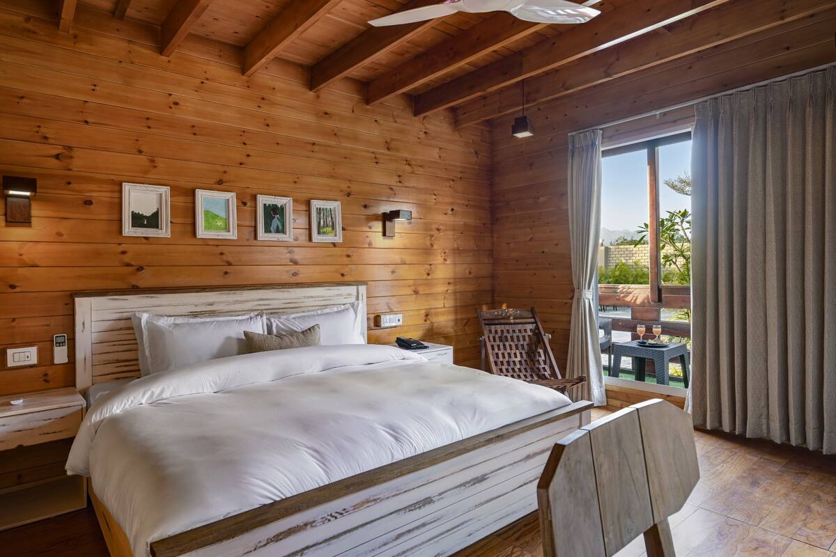 Een houten slaapkamer met een groot bed, een nachtkastje, een stoel en uitzicht op de natuur.