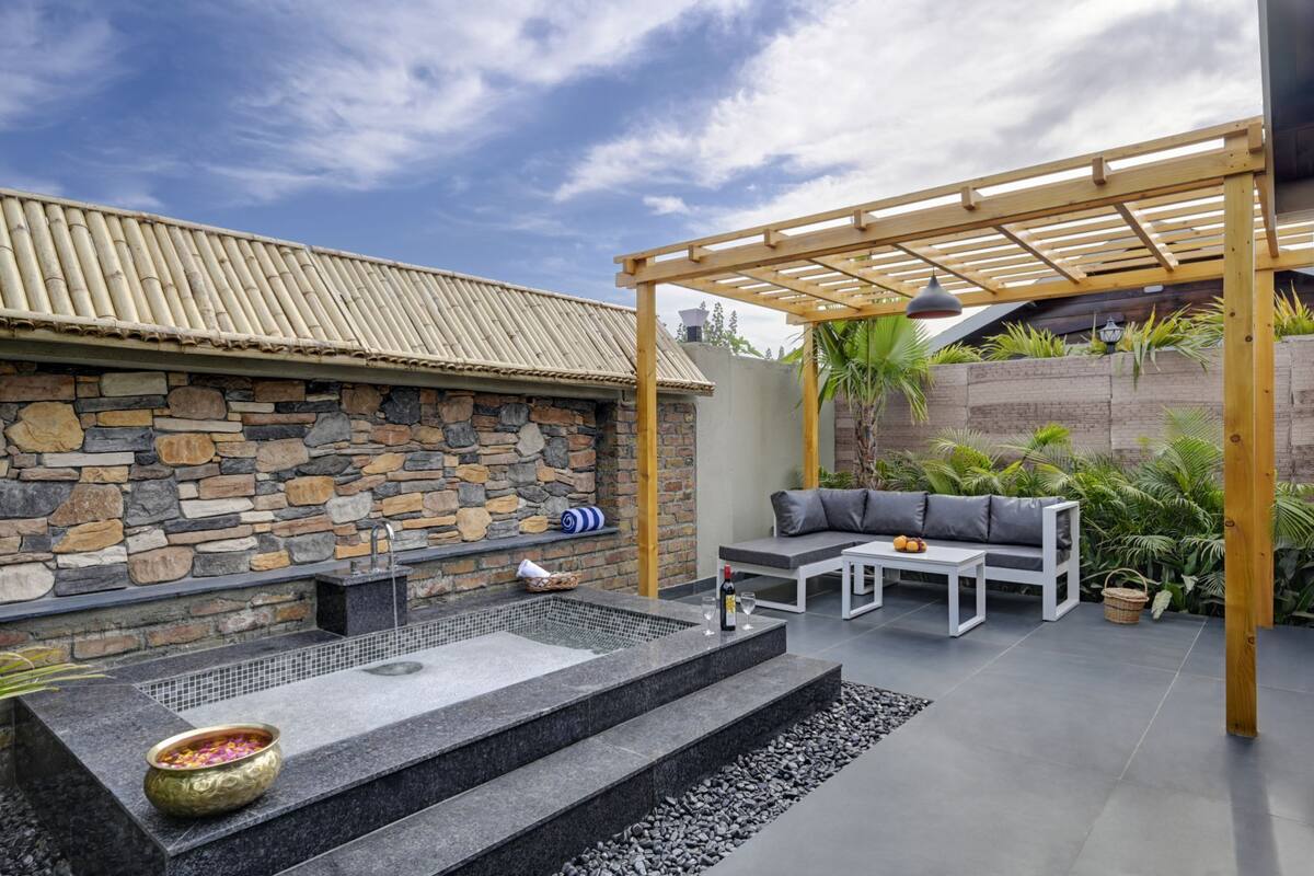 Een stenen muur met een ingebouwde hottub, een houten pergola en buitenmeubilair.