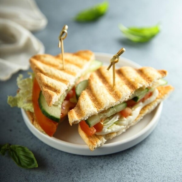 A sandwich with a toothpick, surrounded by lettuce and tomato slices on a plate. - Casawood Resort (Pindwara)