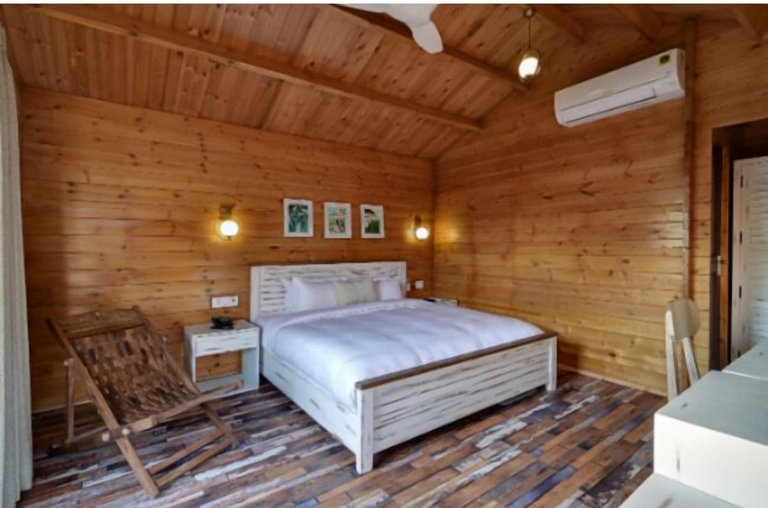 Un dormitorio de cabaña de madera con una cama, mesitas de noche y una silla de madera.