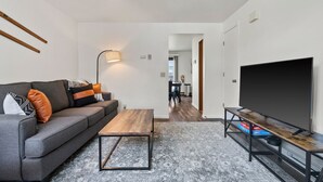Una sala de estar moderna con sofá, mesa de centro, televisor y lámpara.