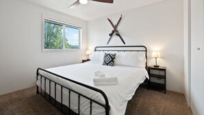 Un dormitorio con cama, ventilador de techo, ventana y un perchero para esquíes en la pared.