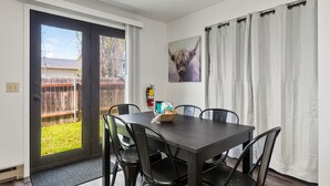 Un comedor con una mesa, sillas, un extintor y vista al patio trasero.