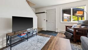 Una sala de estar con televisor de pantalla plana, una mesa de centro de madera, un sofá y un ventanal con vistas.