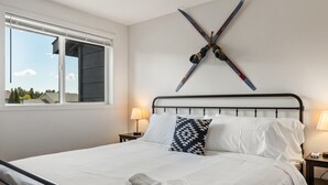 A bed with white linens, a black metal headboard, and a pair of skis mounted on the wall.