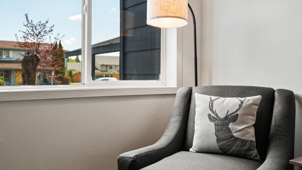 A room with a window, a lamp, and a chair with a decorative pillow.