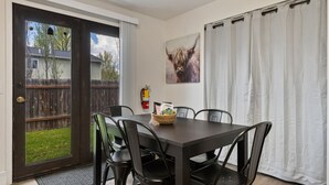 A dining area with a table and chairs, a door with a view to a backyard, a fire extinguisher, and a framed picture on the wall.