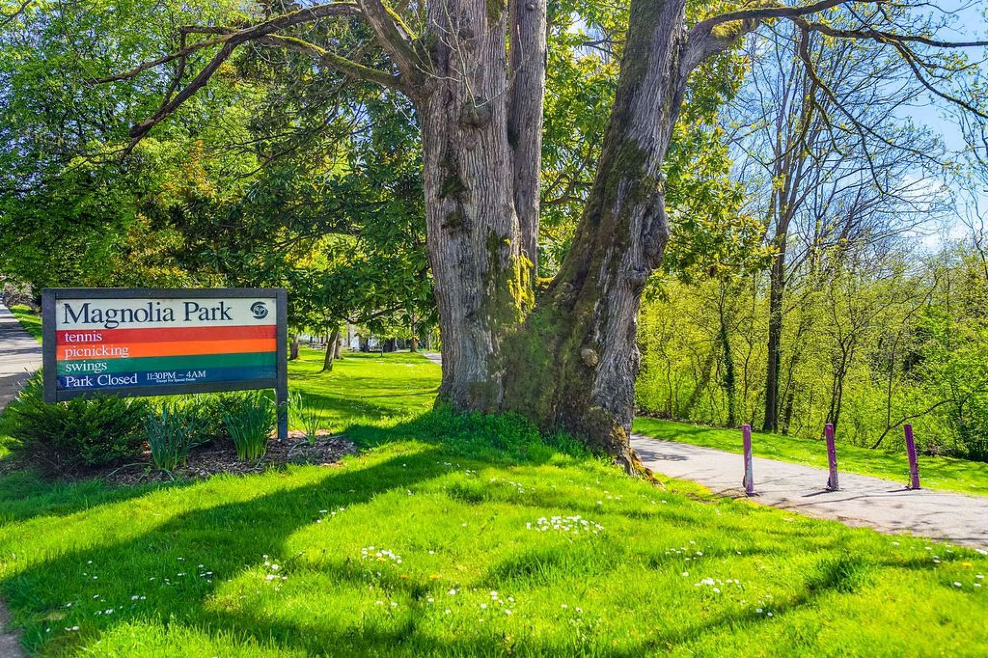 A sign for Magnolia Park indicating amenities like tennis, picnicking, and swings, and mentions park closure times.