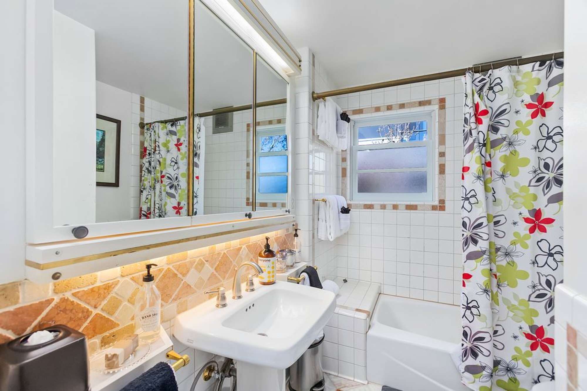 Une salle de bain avec un lavabo blanc, un miroir et un rideau de douche à motifs floraux.