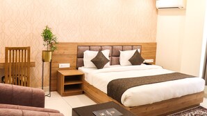 Habitación de hotel con cabecera de madera, mesita de noche, sofá, mesa de centro y planta en maceta.