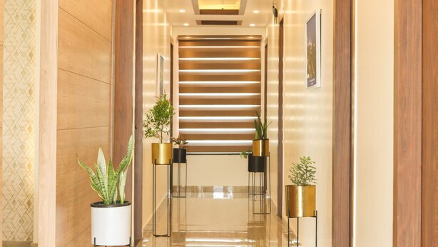 Un moderno vestíbulo de hotel con una escalera de cristal, plantas en macetas y un muro con diseño.