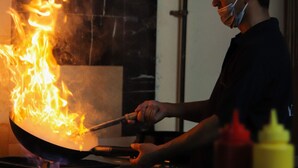 Una persona cocina con un wok sobre una hornilla, rodeada de utensilios de cocina y condimentos.