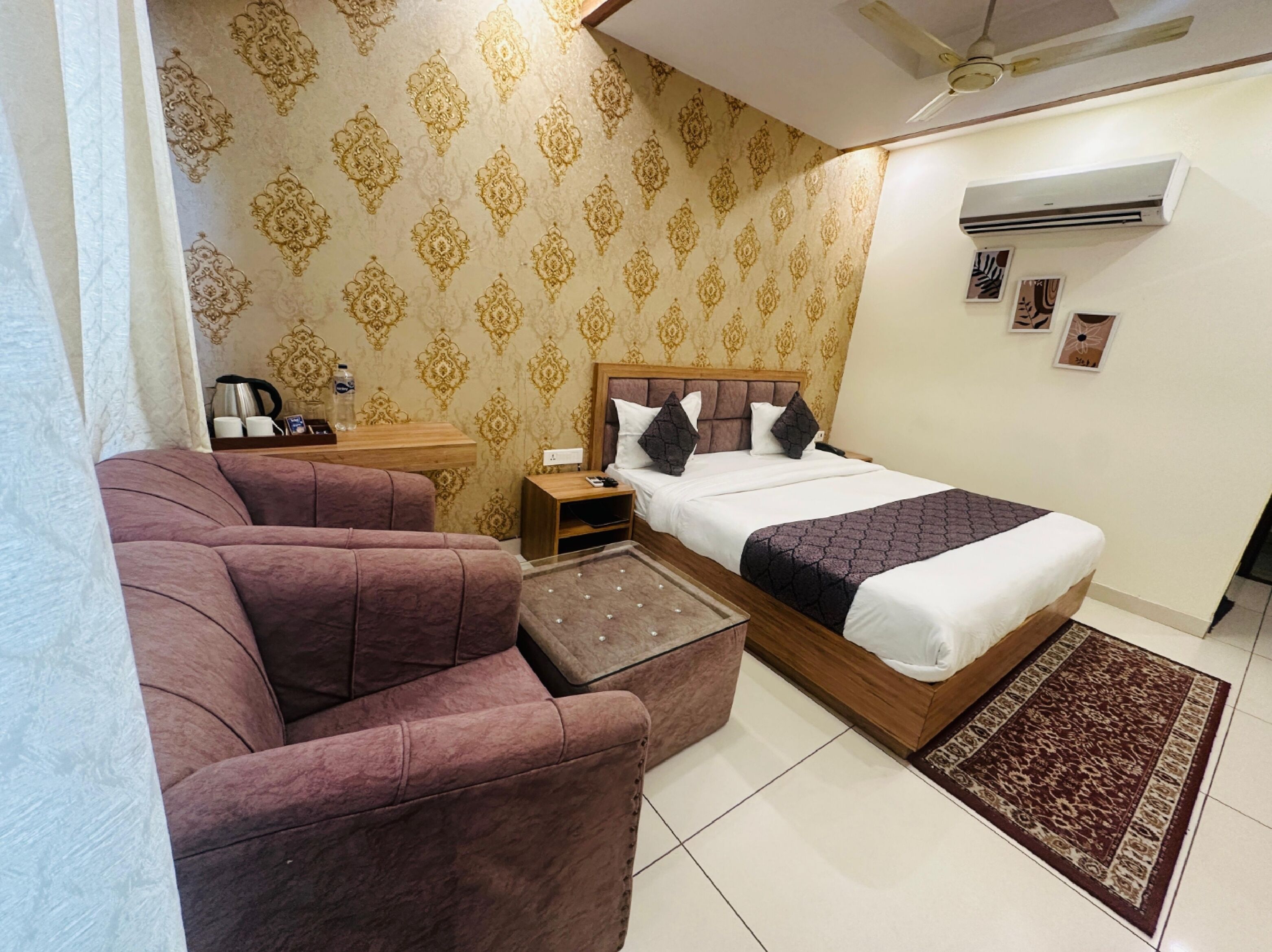 Habitación de hotel con cama, sofá, mesita de noche, cafetera y aire acondicionado de pared.