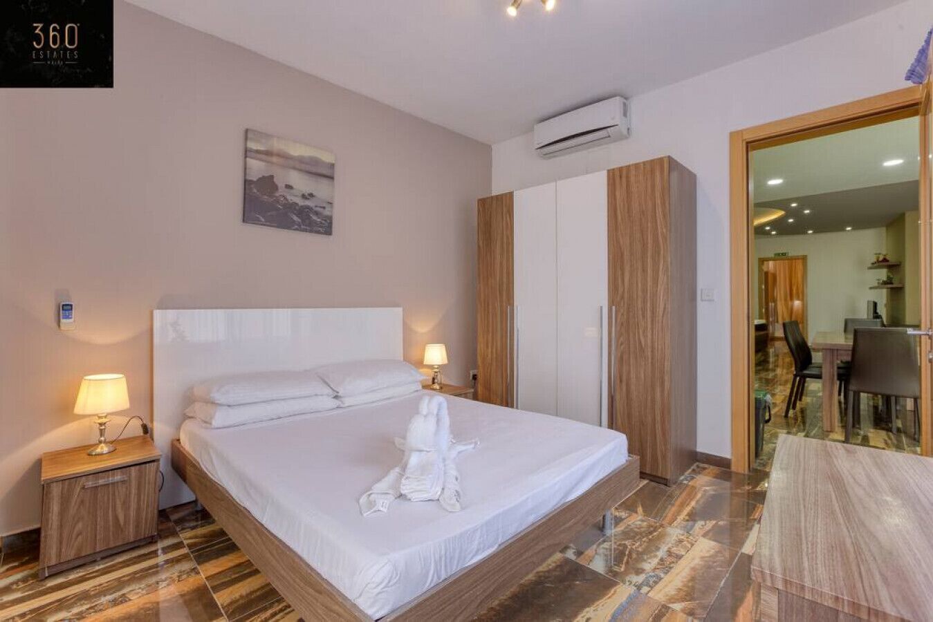 Une chambre d’hôtel avec un grand lit, deux lampes de chevet, un tableau au mur, un appareil de climatisation et une vue sur la salle à manger.