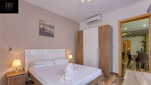 A hotel room with a large bed, two bedside lamps, a painting on the wall, an air conditioning unit, and a view into the dining area. - Central 4BR, massive APT with private POOL & BBQ (Is-Swieqi)