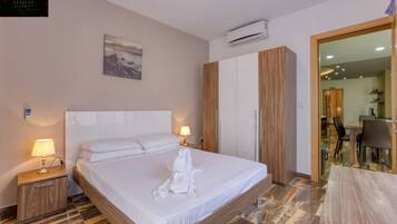 Une chambre d’hôtel avec un grand lit, deux lampes de chevet, un tableau au mur, un appareil de climatisation et une vue sur la salle à manger.