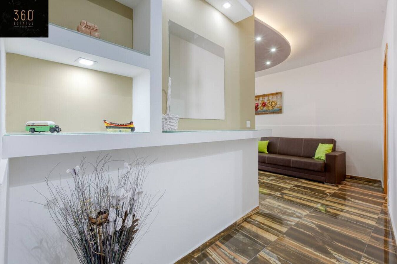 Un espace d’accueil moderne comprenant un canapé, une vitrine et une plante décorative.