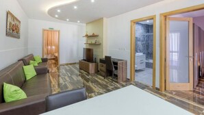 A modern living room with a sofa, a dining table, and a TV. There is a shower area visible through a glass door. - Central 4BR, massive APT with private POOL & BBQ (Is-Swieqi)