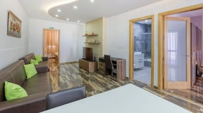 Ein Hotelzimmer mit einer Couch, einem Schreibtisch, einem Sessel, einem Fernseher, einer Dusche und einer Tür zu einem weiteren Raum.