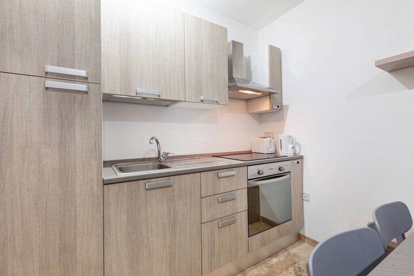 Una cucina moderna con mobili chiari in legno, un lavello in acciaio inossidabile, forno integrato e macchina da caffè.