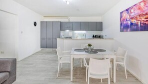 A compact kitchen with grey cabinets, a white dining table with four chairs, and a small island with a microwave.
