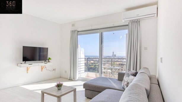 Ein modernes Wohnzimmer mit grauem Sofa, einem kleinen Holztisch und einem flachbildfernseher, der an der Wand angebracht ist.