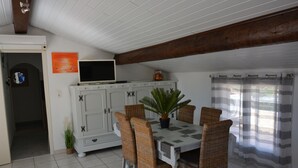 A dining area with a white table, wicker chairs, a potted plant, and a white cabinet with a television on top. - Appartement Dans Villa Piscine ET SPA (SAINT LUCIE DE PORTO VECCHIO)