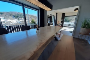 Et moderne spiseområde med et langt bord, stole og udsigt til det fri.