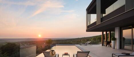 A modern building with a rooftop pool, lounge chairs, and a scenic sunset view.