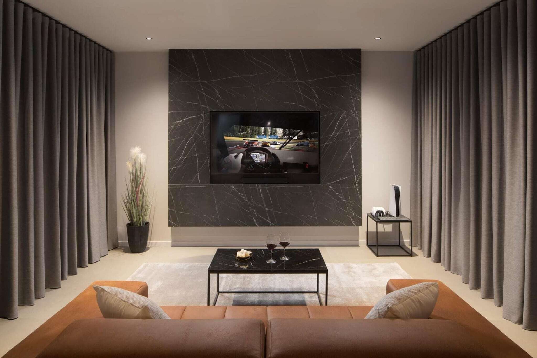 Un salon moderne avec un grand téléviseur à écran plat fixé sur un mur en marbre, une table basse avec deux verres et une plante en pot.