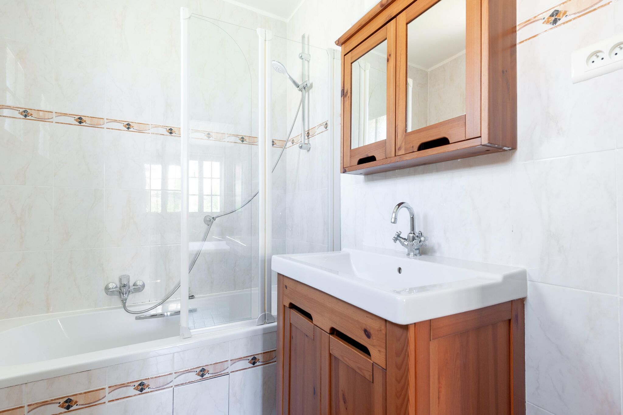 Une salle de bain avec une douche à parois de verre, un lavabo blanc, des meubles en bois et un meuble à pharmacie en bois au-dessus du lavabo.
