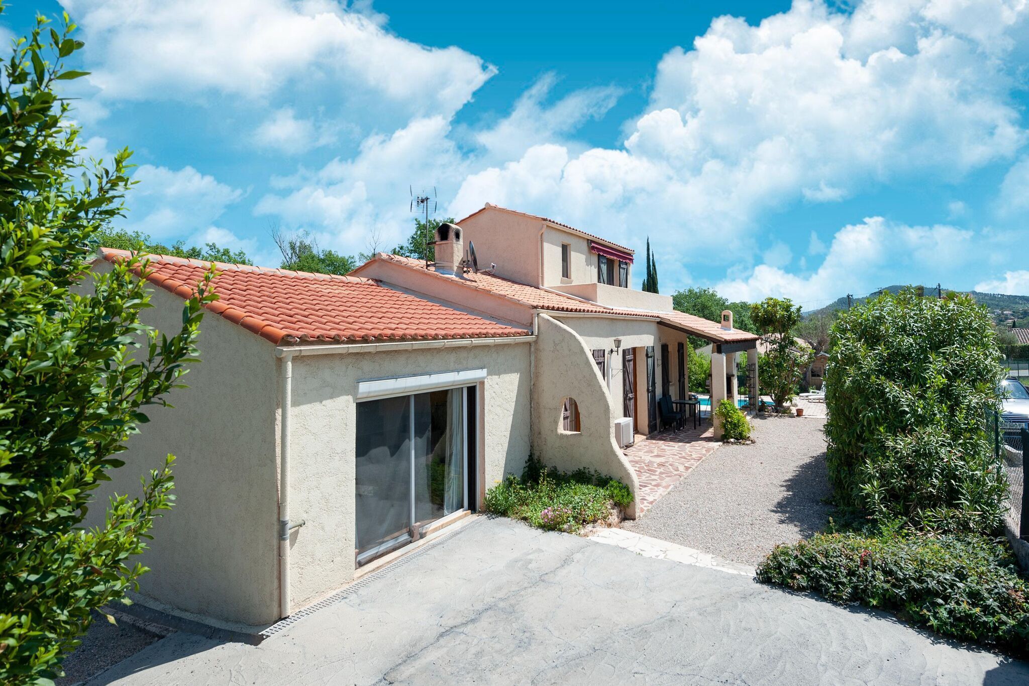A two-story house with a red-tiled roof, a small balcony, and a gravel driveway.
