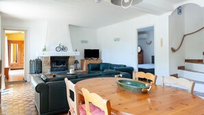 Amplia sala de estar con chimenea, televisor y comedor con mesa y sillas de madera.