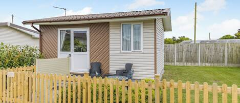 A single-story mobile home with a fenced yard, a patio with outdoor furniture, and a clear sky.